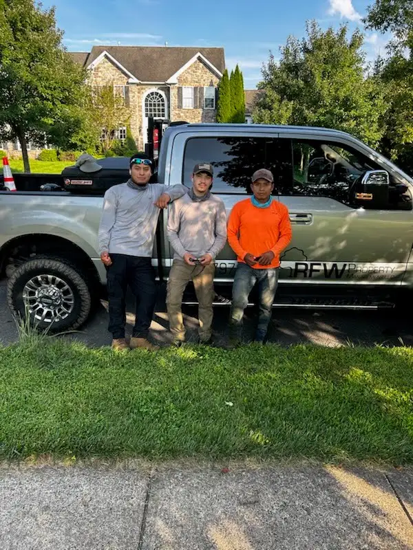 Three RFW crew members stand in front of the RFW pickup truck outside a stone house.